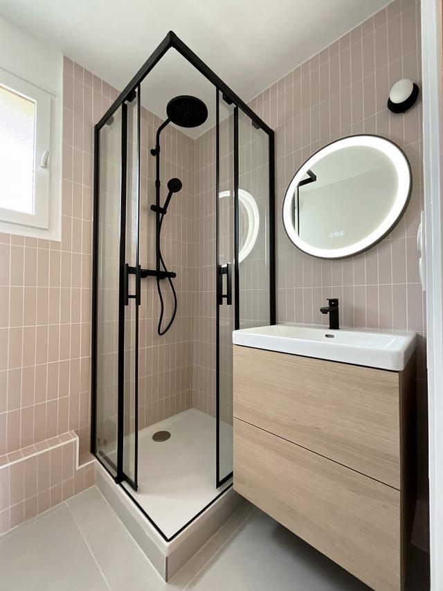Salle de bain avec faïence rose et robinetterie noire.